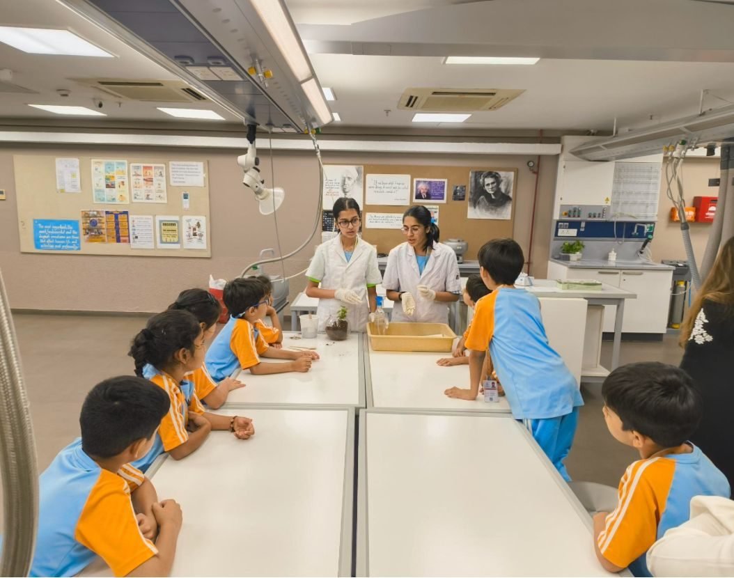 Ariana in a lab coat demonstrating an experiment to a group of young students at a lab bench
